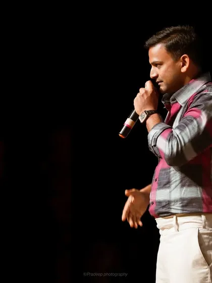 A profile shot of actor Dhananjaya speaking on stage. The dark background makes the subject stand out, creating a powerful and focused portrait.