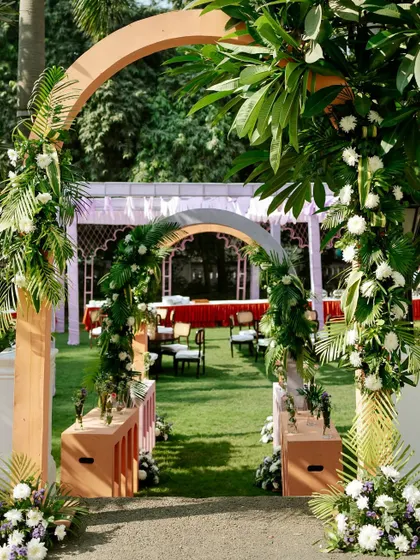 A lush green entranceway for the Mehendi, with simple wooden arches wrapped in tropical leaves and white flowers, creating a natural and organic feel.