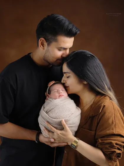 The complete family. A father’s gentle kiss on the mother’s forehead while she holds their newborn creates a portrait filled with love, protection, and tenderness.