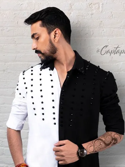 This image showcases an edgier style of men's fashion photography. Shot against a textured brick wall in the studio, the focus is on the unique design of the split black-and-white shirt and the model's strong profile.