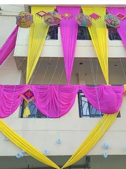 The balcony of a building decorated with pink and yellow drapes and colorful Rajasthani umbrellas for a Mehendi function.