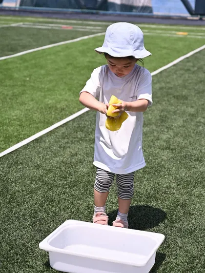 This playgroup child is engaged in a water-based activity at our sports meet. Squeezing a sponge is a fun way to build hand strength and develop hand-eye coordination.