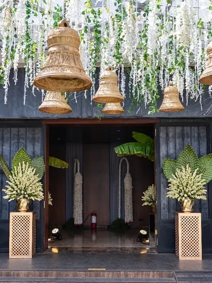 The entrance to a wedding venue, decorated with hanging temple bells and traditional floral arrangements.