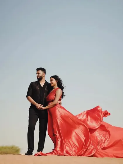 A breathtaking desert pre-wedding shoot. The vibrant red of her infinity dress flows beautifully in the wind, creating a stunning contrast with the sandy landscape.