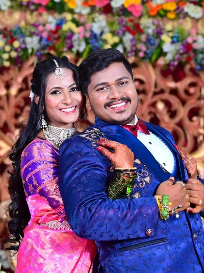 A happy, classic portrait of the newly married couple at their wedding reception, posing against a vibrant floral backdrop.