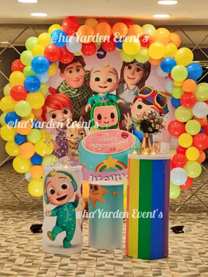 A full and festive Cocomelon themed birthday circle. The round backdrop features the whole Cocomelon family, surrounded by a rainbow balloon garland and themed cake stands.