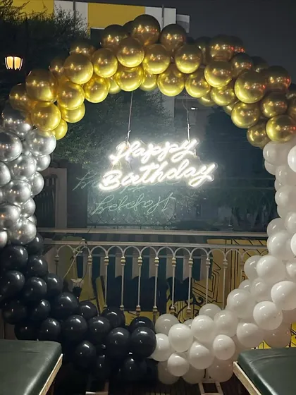 A stylish outdoor birthday photo booth on a balcony. The circular balloon arch in black, white, and gold chrome balloons creates a modern and chic look.