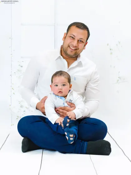 A proud father sits with his baby on his lap, both looking at the camera. This simple and clean portrait beautifully captures the father-son bond.