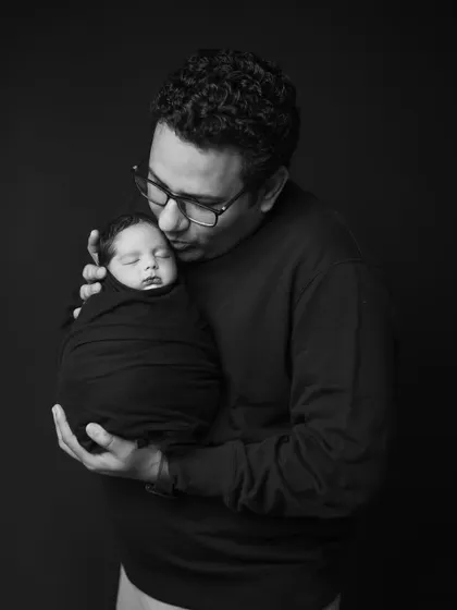 A quiet moment between father and child. This intimate black and white portrait captures a dad gently kissing his swaddled newborn, a memory he will treasure forever.