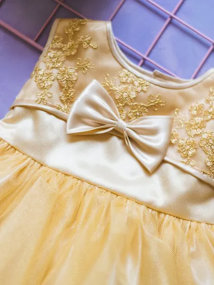This golden-yellow dress features beautiful floral embroidery on the bodice, perfectly complemented by a satin bow. It’s a detail that adds a touch of luxury and charm.