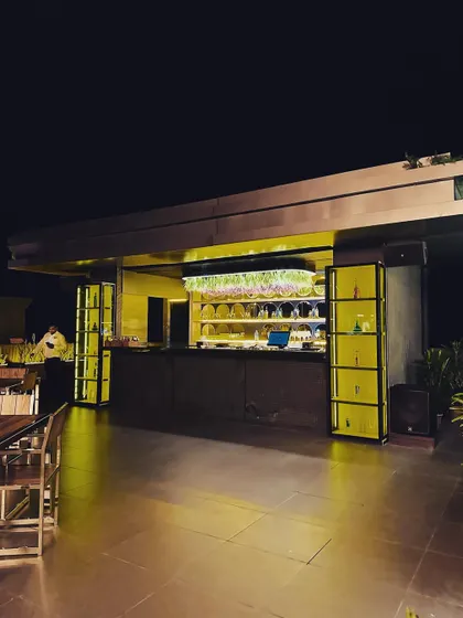 A wide view of the outdoor bar, showcasing its full length and the dramatic effect of the under-counter and shelf lighting against the night sky.