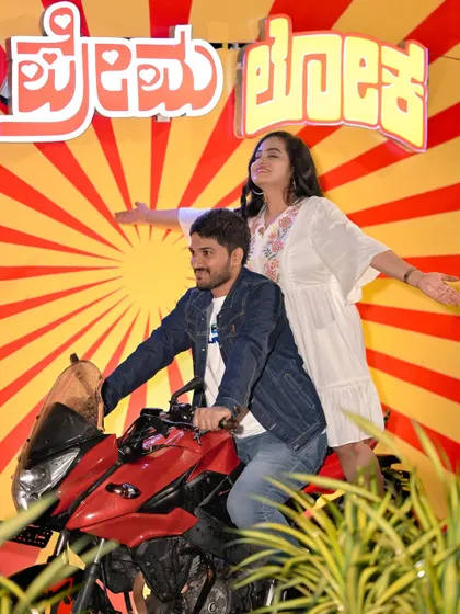 A fun, retro-style shot with our 'Premaloka' movie backdrop and a motorcycle, perfect for film-loving couples.