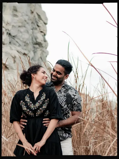 A joyful, candid shot of the couple laughing together in a natural, rustic setting.