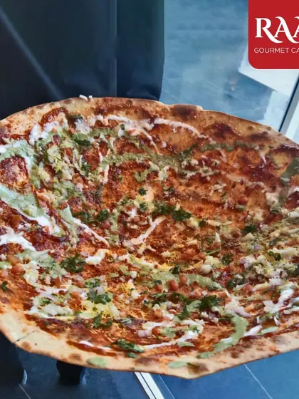 A guest holding up my signature Kadak Roomali, a massive, crispy flatbread topped with sauces and savoury garnishes. It's an interactive and delicious centerpiece for any party.