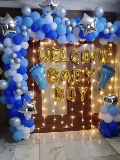 A simple and sweet decoration for welcoming a baby boy. The backdrop features 'Welcome Baby Boy' foil balloons, a fairy light curtain, and a blue and white balloon frame.