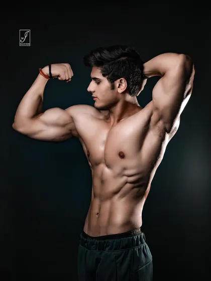 An alternate take on the classic bicep flex, captured from a profile angle to showcase the full curvature and size of the arm muscles. This is a testament to hard work and dedication in the gym.