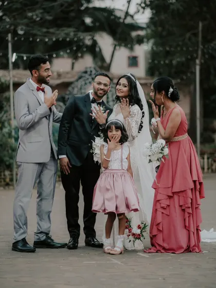 A fun family portrait with the couple showing off their wedding rings, surrounded by their loved ones.