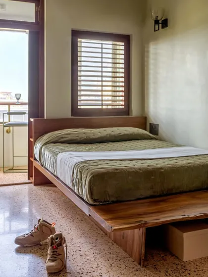 A bedroom in Apartment 5026, where a simple wooden bed and reclaimed terrazzo floor create a warm, vintage feel.