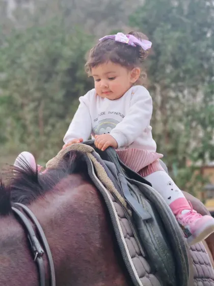 A young child looks down with curiosity while seated on a horse, a moment of discovery and connection.
