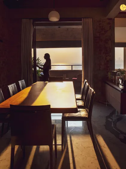 Golden hour at 'The Canvas' project in Marine Drive. The setting sun casts long shadows across the dining area, highlighting the texture of the exposed brick and the warmth of the wooden table, showcasing how light transforms a space throughout the day.