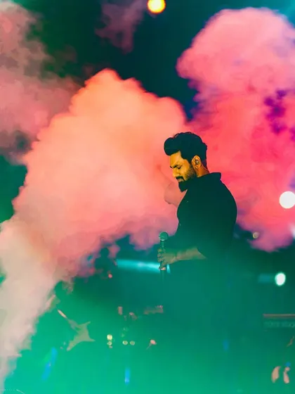 An atmospheric shot of Mithoon on stage, surrounded by colored smoke, during the Shor Fest concert in Daman.