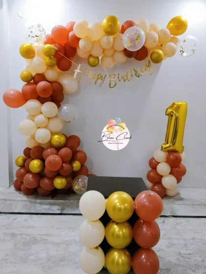 A simple L-shaped balloon arch in warm tones for a first birthday celebration at home.