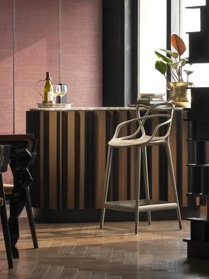 The bar area in the Caitriona apartment, featuring a standalone bar with a white onyx top and wallpaper-clad shutters. A playful Kartell bar chair adds a touch of modern design to this sophisticated entertaining space.