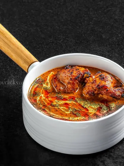 A chicken curry dish served in a modern white pot, with a focus on the rich texture of the gravy.