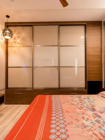 A bedroom from the Murlis' home, showcasing a large sliding door wardrobe, a cozy bed, and a sleek TV unit, all tied together with warm wood tones and a modern aesthetic.