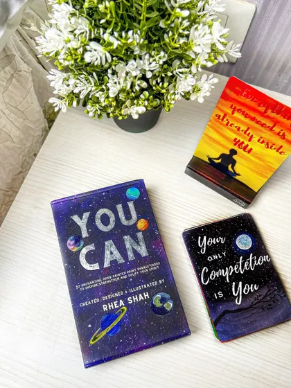 A cozy, lifestyle shot of motivational card decks on a bedside table with flowers. This helps customers imagine incorporating these products into their daily routines.
