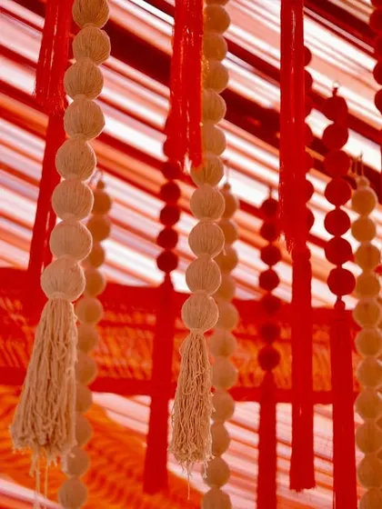 A close-up of the ceiling decor, showing the intricate details of the hanging tassels and beads against the backdrop of red and orange drapes. Fine details are our expertise.