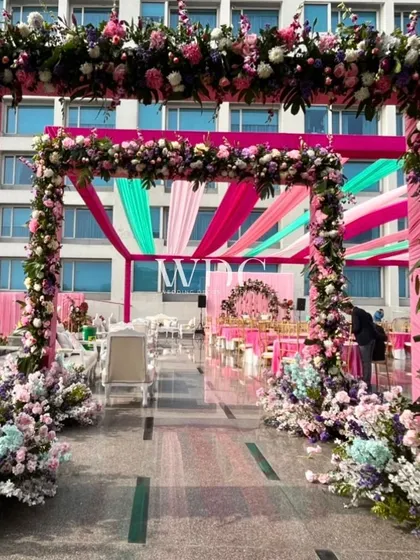A grand floral entrance for a pastel-themed Mehendi. The arch is covered in a profusion of pink, purple, and blue flowers, creating a stunning welcome for guests.