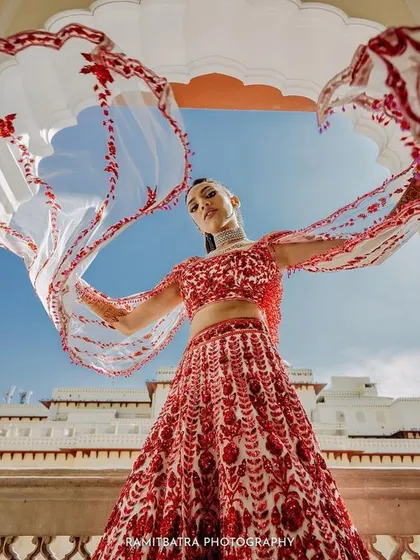 A dynamic shot of the bride twirling her intricately embroidered dupatta against the backdrop of the palace and a clear blue sky.