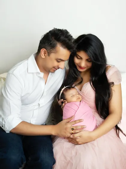 A tender moment with the family seated together, admiring their sleeping baby. The mother's pink dress coordinates beautifully with the baby's swaddle.