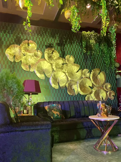 A lounge area within the enchanted forest theme, featuring a wall of golden lily pad sculptures and deep green sofas.