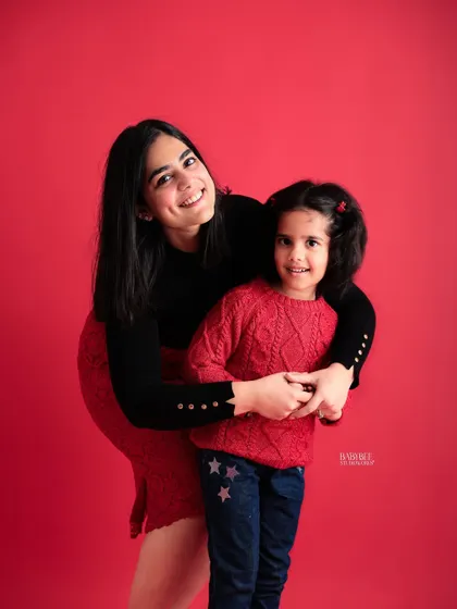 A mother and daughter duo against a vibrant red backdrop. This portrait is full of warmth and happiness, highlighting their cheerful connection.