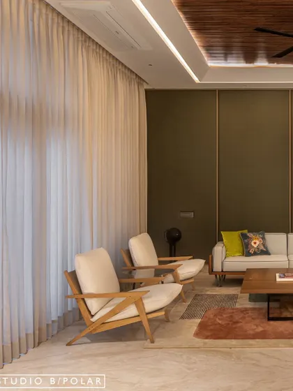 Sheer curtains diffuse natural light, creating a soft and airy feel that balances the deep green of the walls. The clean lines of the armchairs add to the modern aesthetic of the lounge.