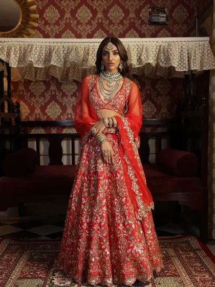 A full-length shot capturing the vintage charm of this red lehenga. The model's pose and the opulent setting work together to create a look that feels like it's from a classic Indian painting.