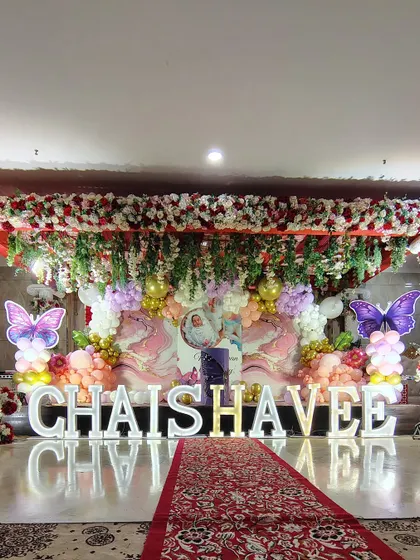 A full view of the grand 'CHAISHAVEE' birthday stage. The red carpet runner leads guests towards the magnificent backdrop, which combines florals, balloons, and personalized lighting for a complete venue transformation.