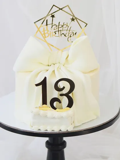 An elegant cake to welcome the teenage years. This design features a large, beautifully crafted white fondant bow, making it a sophisticated choice for a 13th birthday.