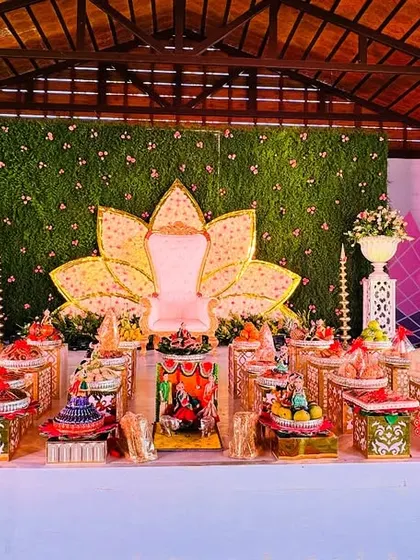 A beautiful platter arrangement for a naming ceremony with a lotus-themed stage. The colors and elements of the platters are chosen to match the pink and gold tones of the backdrop.