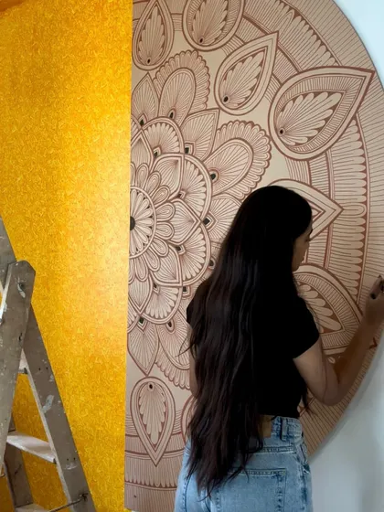 Working on a half mandala mural next to a textured yellow wall. The contrast between the simple line work and the bright color makes the art pop.