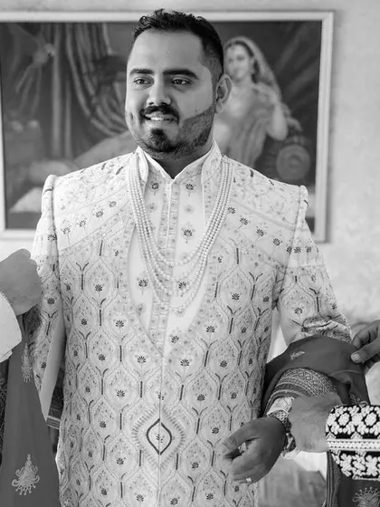 A classic black and white shot of the groom getting help with his sherwani. These moments of camaraderie with friends and family are an essential part of the day.