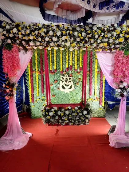 A floral and fabric backdrop for a naming ceremony, featuring a Ganesha cutout and a decorated cradle.
