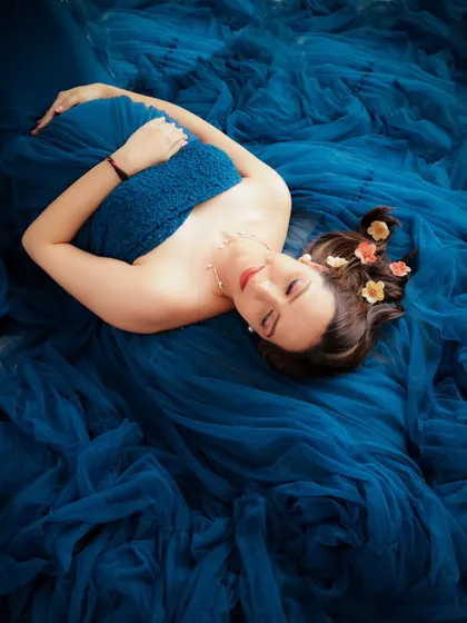 A dreamy overhead shot of a mom-to-be lying in a sea of blue tulle, with small flowers in her hair. An artistic and beautiful portrait.
