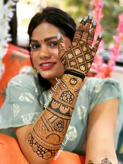 A happy bride showing off her intricate henna. The design features a mix of checks, floral patterns, and traditional motifs covering her hand and arm.