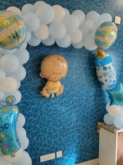 A simple wall decoration for a baby boy's arrival, featuring a light blue balloon arch and cute baby-themed foil balloons.