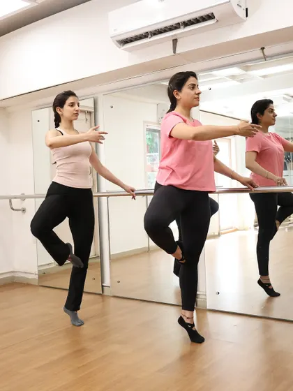 An instructor guides a member through a graceful barre movement, highlighting the personalized attention in our small group classes.