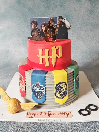 "Happiness can be found, even in the darkest of times." A 10-inch tall, two-tier Harry Potter cake, featuring the four house banners, a golden snitch, and Harry's glasses, all made from fondant.