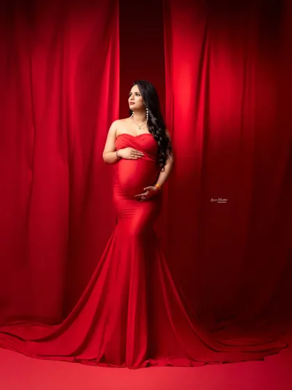 A vision in red. This full-length portrait captures the grandeur of the flowing red gown against a dramatic, theatrical curtain backdrop.